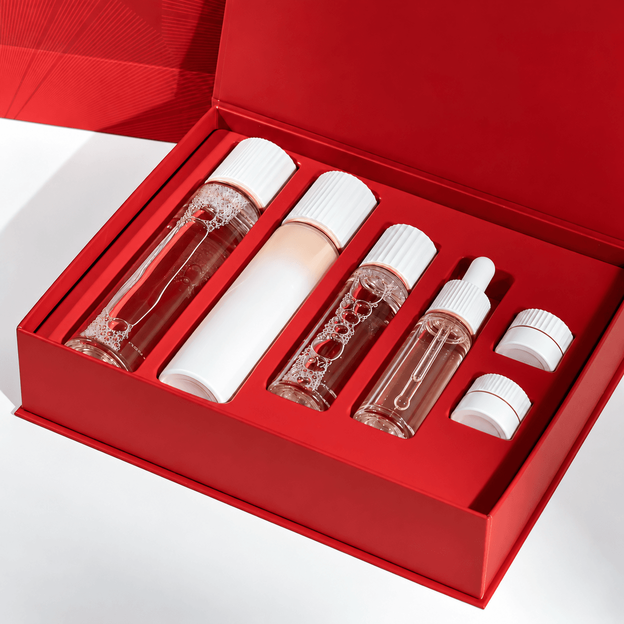 Red luxury skincare gift box featuring toner bottles, a serum dropper bottle, and matching cosmetic containers