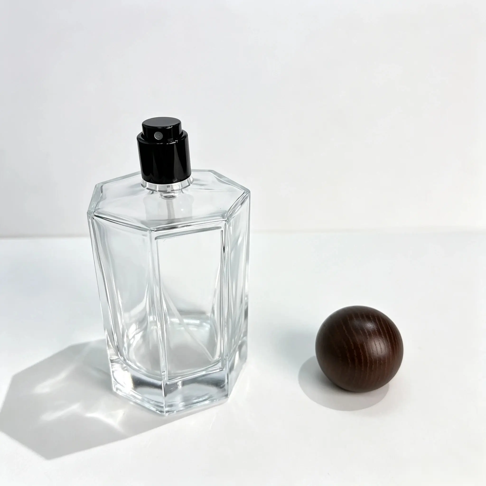 100ml octagonal glass perfume bottle shown bare with the walnut wood ball-shaped outer cap displayed separately beside the bottle