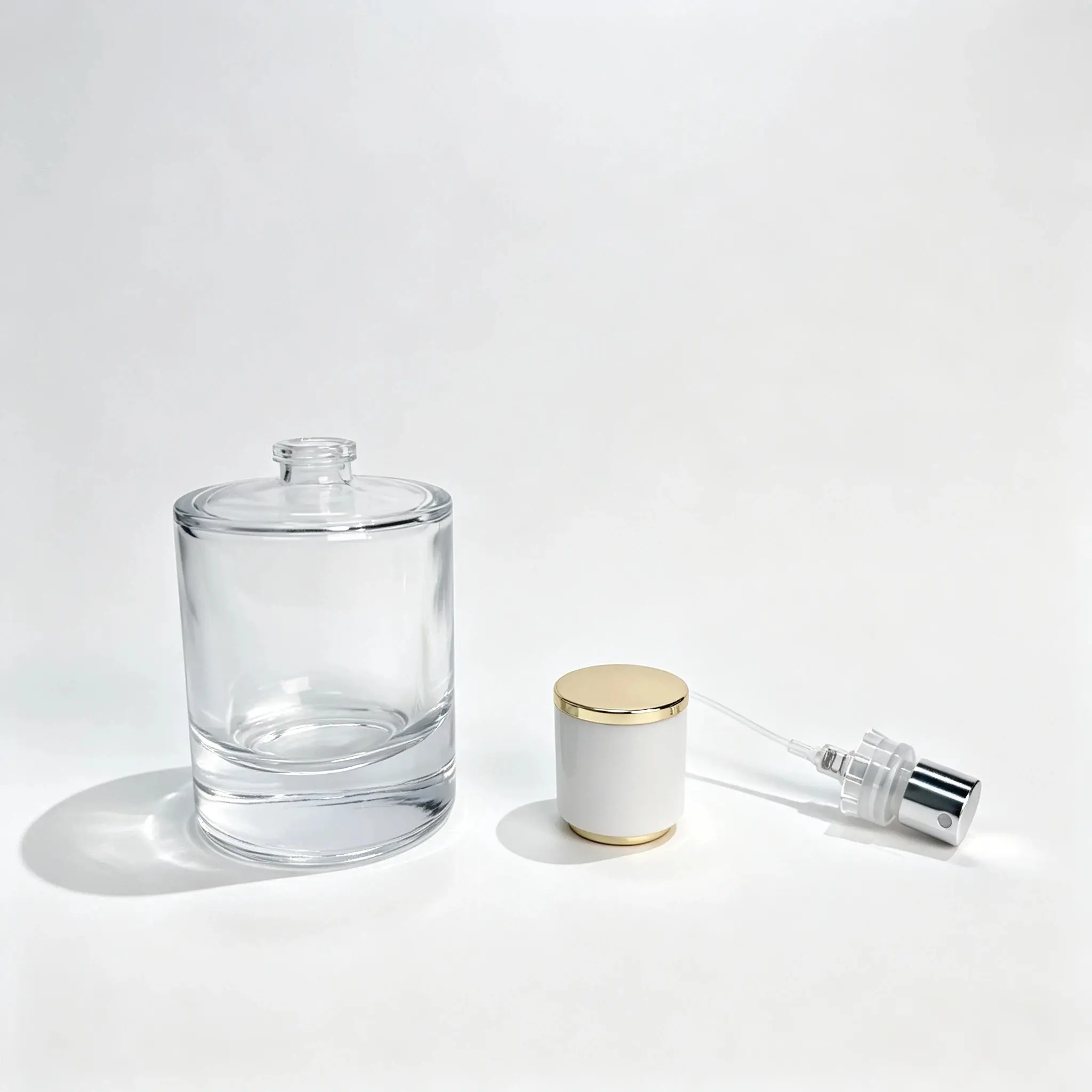 50ml Perfume Bottle with Separate Cap and Crimp Sprayer 50ml round cologne bottle shown with the white and gold cylindrical cap and crimp sprayer positioned separately beside the bottle