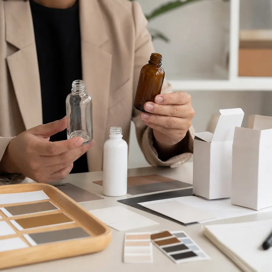 Comprador revisando muestras de color de botellas de vidrio cosmético con estuches de cartón