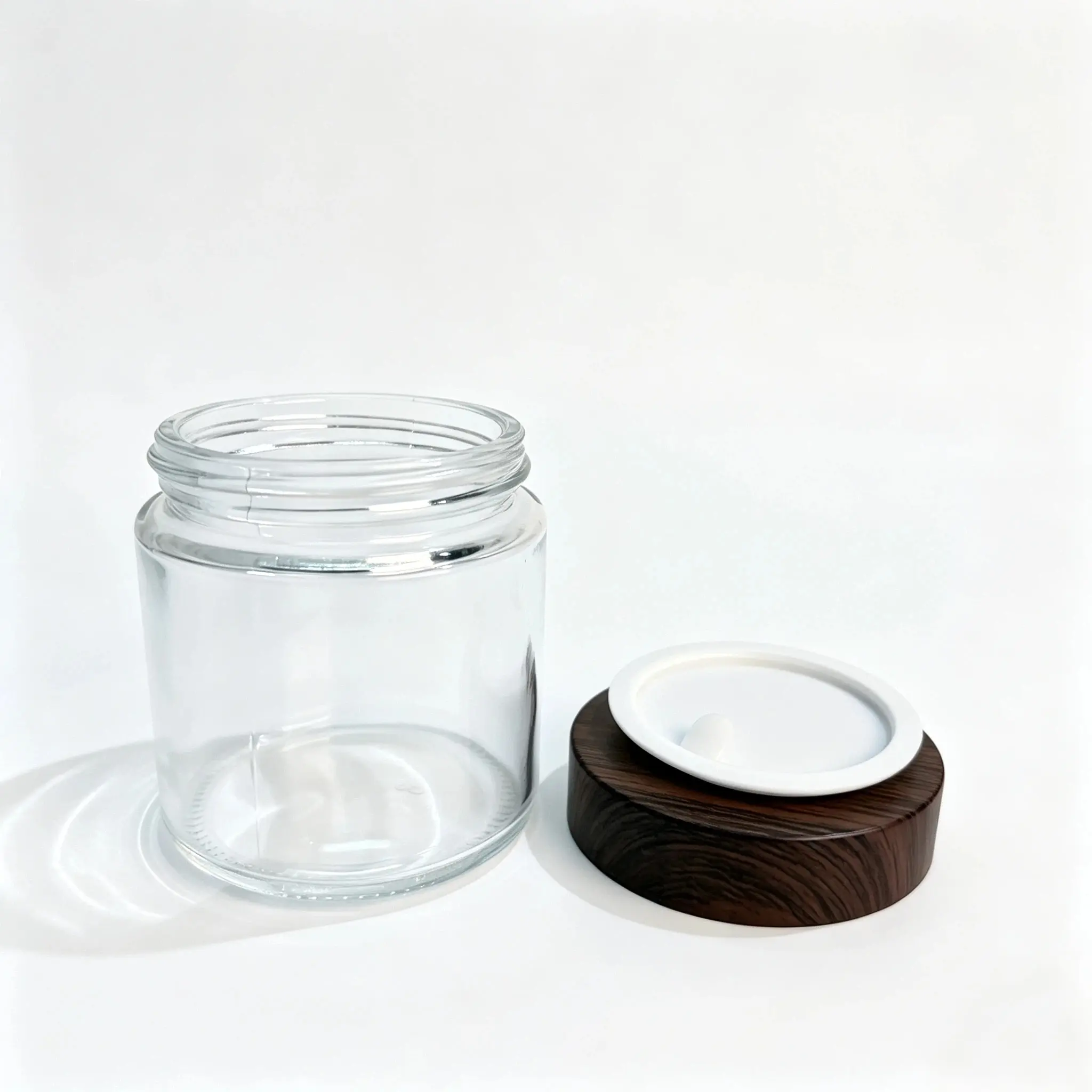 100g Boião de Creme de Vidro Transparente sem Tampa e Fecho Boião de creme de vidro transparente de 100g sem tampa apresentado ao lado da respetiva tampa de rosca com efeito madeira, mostrando a abertura de vidro e os componentes de fecho separados.