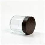 Side view of the 100g clear glass cream jar showing its transparent glass body profile and wood-grain screw-cap closure for skincare packaging.