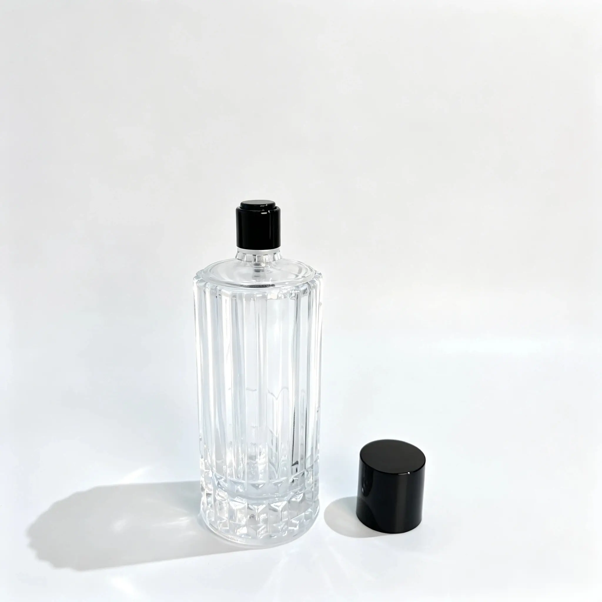 100ml Flacon de parfum colonne cannelée, capot retiré Flacon de parfum colonne cannelée de 100ml sans capot, avec son capot amovible placé à côté du flacon, montrant le corps cylindrique et l'ensemble supérieur apparent.