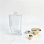 Uncapped 100ml rectangular perfume bottle displayed alongside its separate fragrance sprayer, dip tube, and cap components for packaging assembly reference.