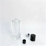 Uncapped 100ml ribbed perfume bottle with its fragrance sprayer, dip tube, and cap arranged separately beside the bottle to show the packaging components.