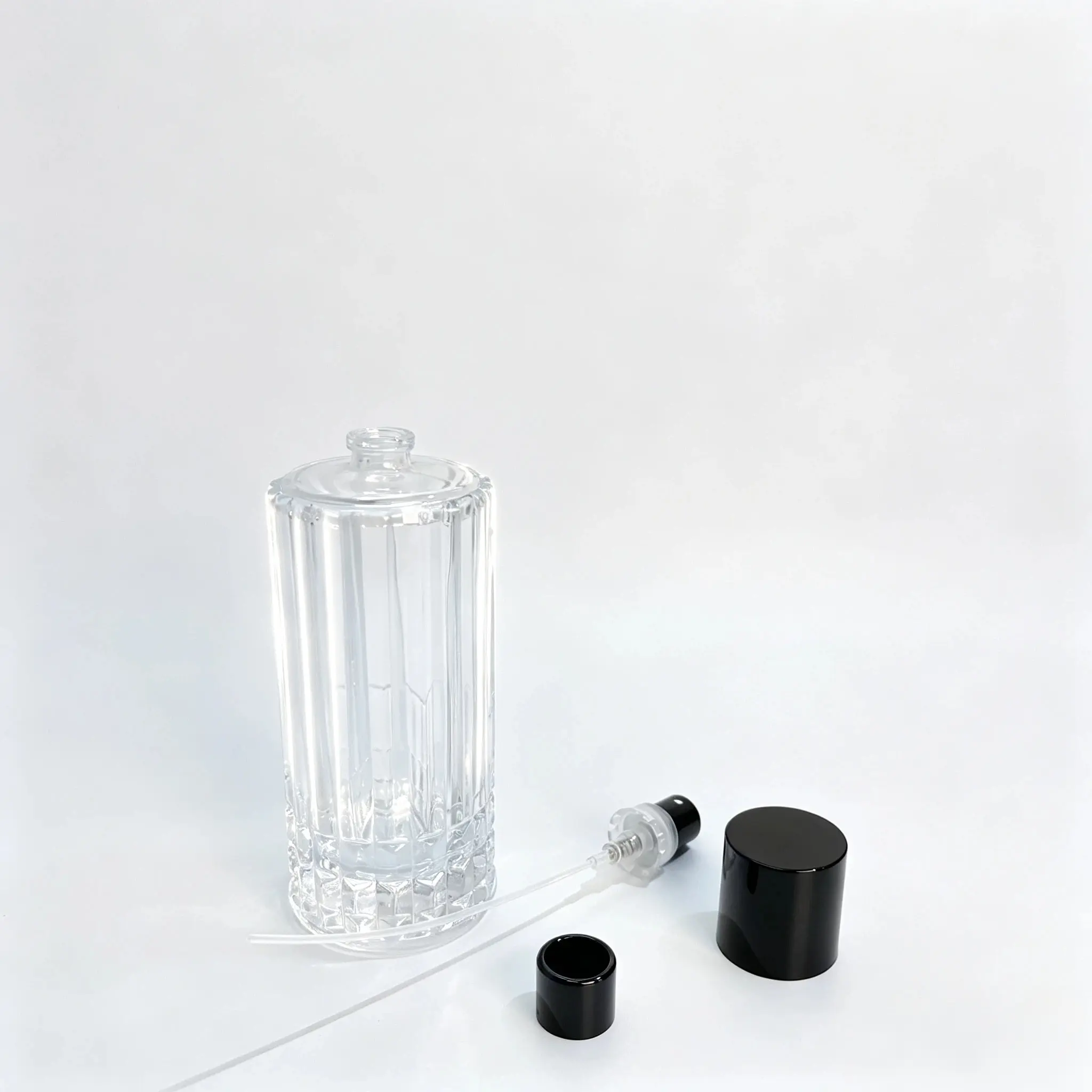 100ml Flacon de parfum nervuré avec vaporisateur et composants du tube plongeur Flacon de parfum nervuré de 100ml sans capot, avec son vaporisateur de parfum, son tube plongeur et son capot disposés séparément à côté du flacon pour montrer les composants de l'emballage.