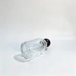Uncapped 100ml round perfume bottle lying on its side with the bottle base visible, showing the lower body profile and bottom structure.