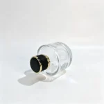 Side-lying view of the 100ml short round perfume bottle with its decorative cap visible, highlighting the bottle's low cylindrical profile and thick base.