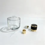 Uncapped 100ml short round perfume bottle displayed with its separate sprayer, dip tube, and decorative cap for fragrance packaging component selection.