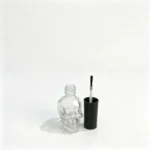 15ml skull-shaped glass nail polish bottle displayed together with its cap and nail polish applicator brush.