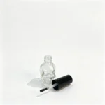 Uncapped 15ml skull-shaped glass nail polish bottle displayed alongside a separate cap and applicator brush.