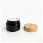 Black glass cosmetic cream jar with its matching bamboo screw cap, showing the container and closure combination for 30g skincare packaging.