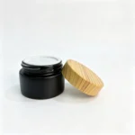 30g black glass cosmetic cream jar displayed with its bamboo screw cap and separate pull-tab lid component for packaging assembly reference.