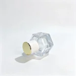 Side-lying view of the 30ml hexagonal glass perfume bottle highlighting the white cylindrical cap, gold-colored top, and geometric bottle profile.