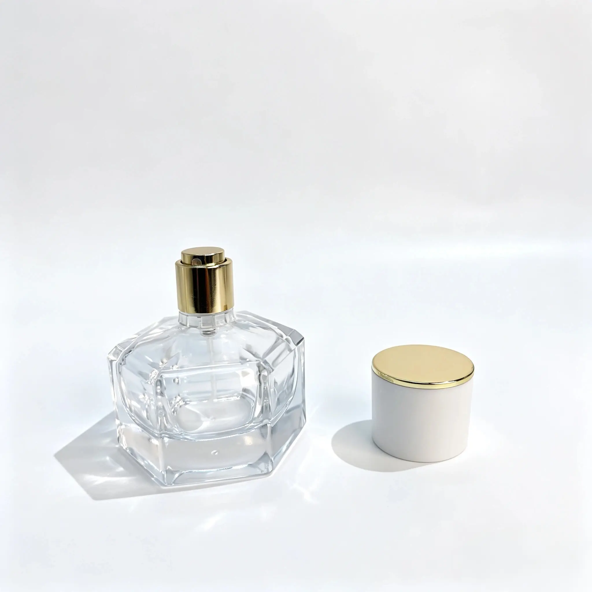 30ml زجاجة عطر زجاجية سداسية – عرض مع إزالة الغطاء الأبيض والذهبي 30ml زجاجة عطر زجاجية بقَطع سداسي مع غطائها الأسطواني الأبيض وقمتها الذهبية اللون وقد أُزيل الغطاء ووُضع بجانب الزجاجة.