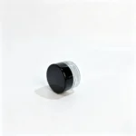 Side view of the 3g clear glass cream sample jar showing its compact glass body and black screw cap profile.