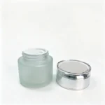 Additional component view of the 50g frosted glass cosmetic jar and silver cap, presenting the glass body and matching closure for packaging selection.