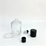 Kapağı çıkarılmış 50ml silindirik parfüm şişesi, ayrı parfüm spreyi, dip tüpü ve dekoratif kapak bileşenlerinin yanında sergilenmektedir.