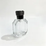 Side profile of the 50ml octagonal perfume bottle showing its 32 mm body depth and the proportions of the assembled black coil-design cap.