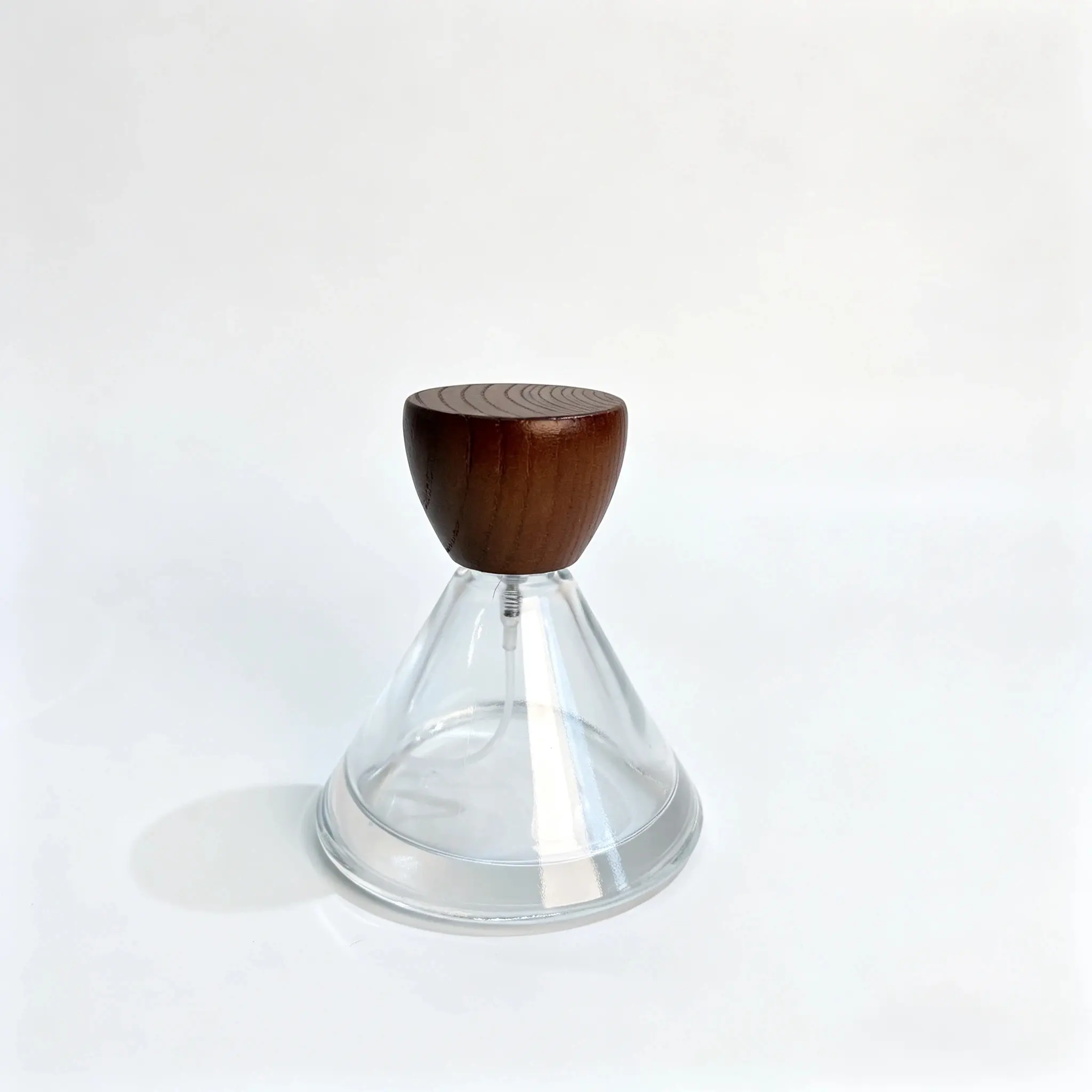 Front view of the 50ml wide round perfume bottle with its conical wooden cap assembled on the short rounded body.