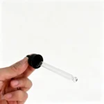 Handheld side view of the black screw cap glass dropper showing the rubber bulb, ribbed closure profile, and transparent glass pipette