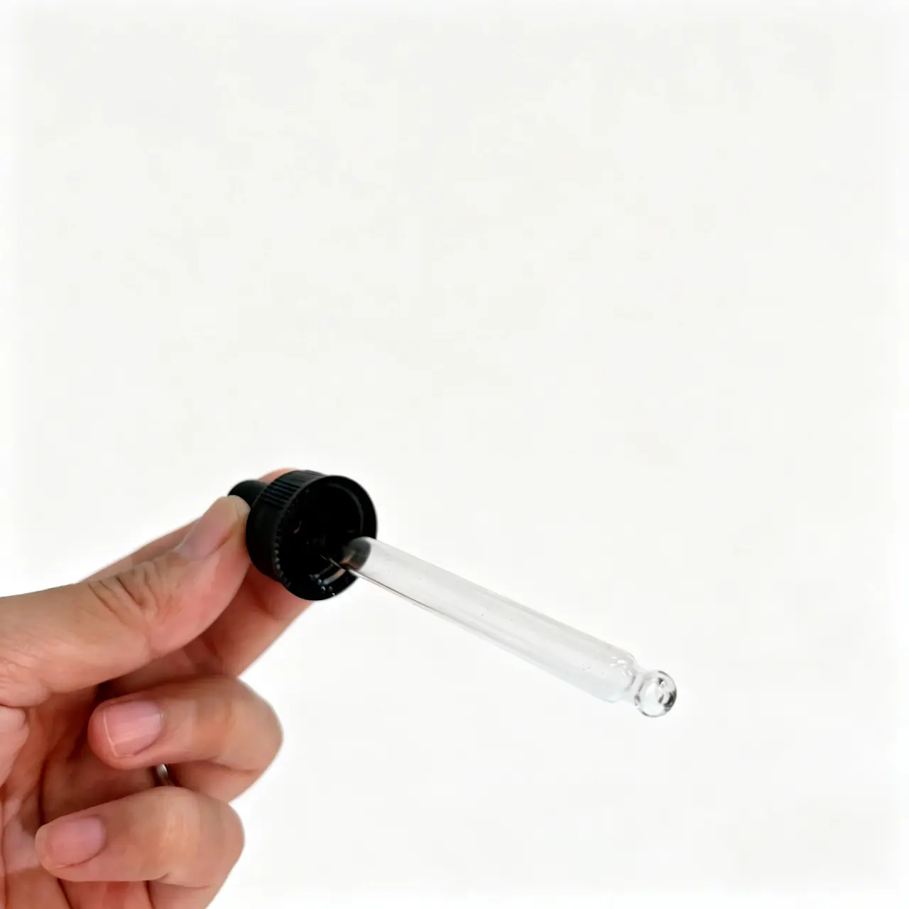 Vue de côté du compte-gouttes pour huile essentielle à bouchon vissé noir Vue de côté tenue en main du compte-gouttes en verre à bouchon vissé noir montrant la poire en caoutchouc, le profil de fermeture nervuré et la pipette transparente