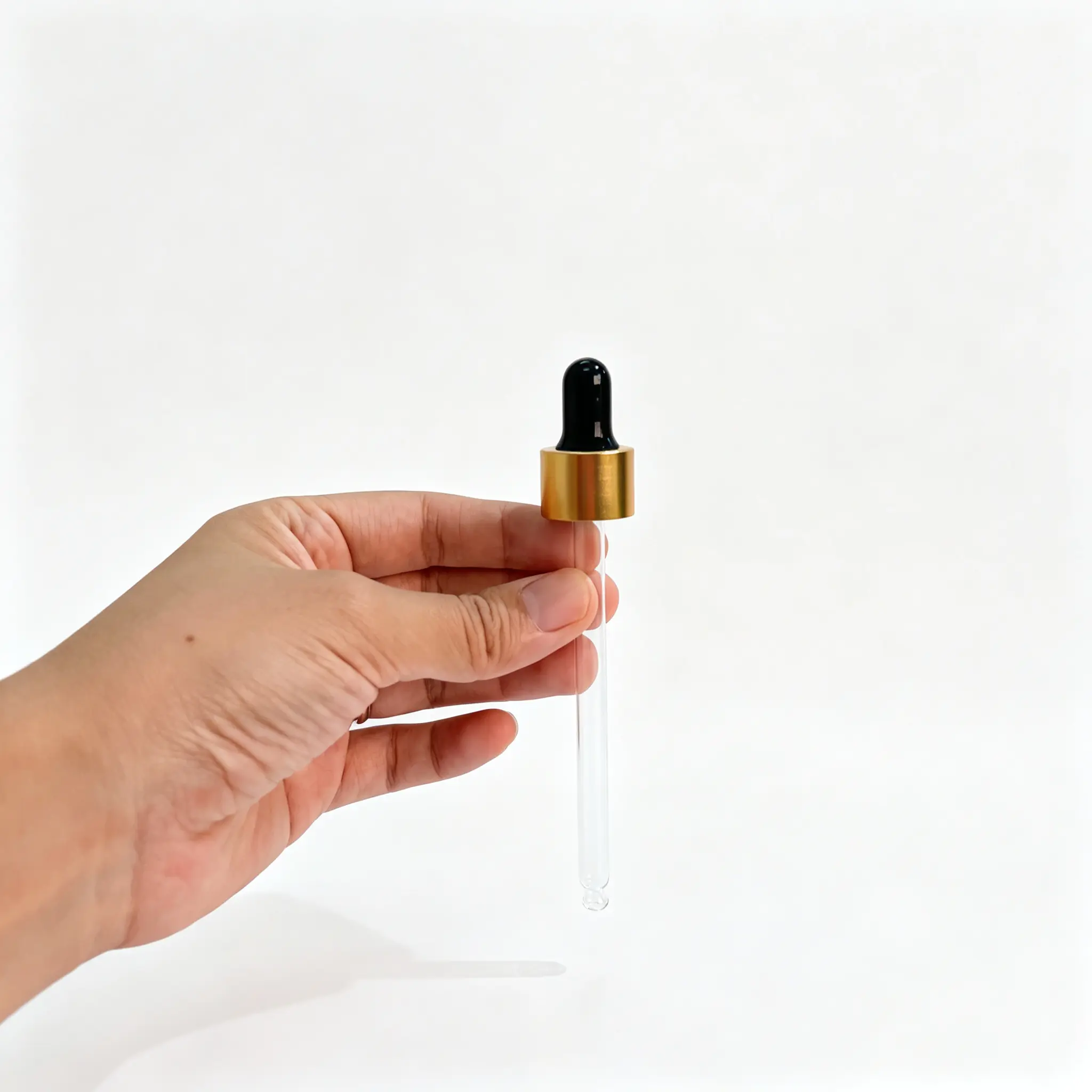 Conta-gotas de vidro com aro de alumínio dourado visto na mão Conta-gotas de vidro com aro de alumínio dourado segurado na mão, mostrando a pera de borracha preta, o aro dourado e a pipeta transparente completa