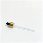 Perfil lateral do conta-gotas de vidro com colar de alumínio dourado mostrando o bulbo de borracha preto, o colar metálico e a pipeta de vidro transparente completa