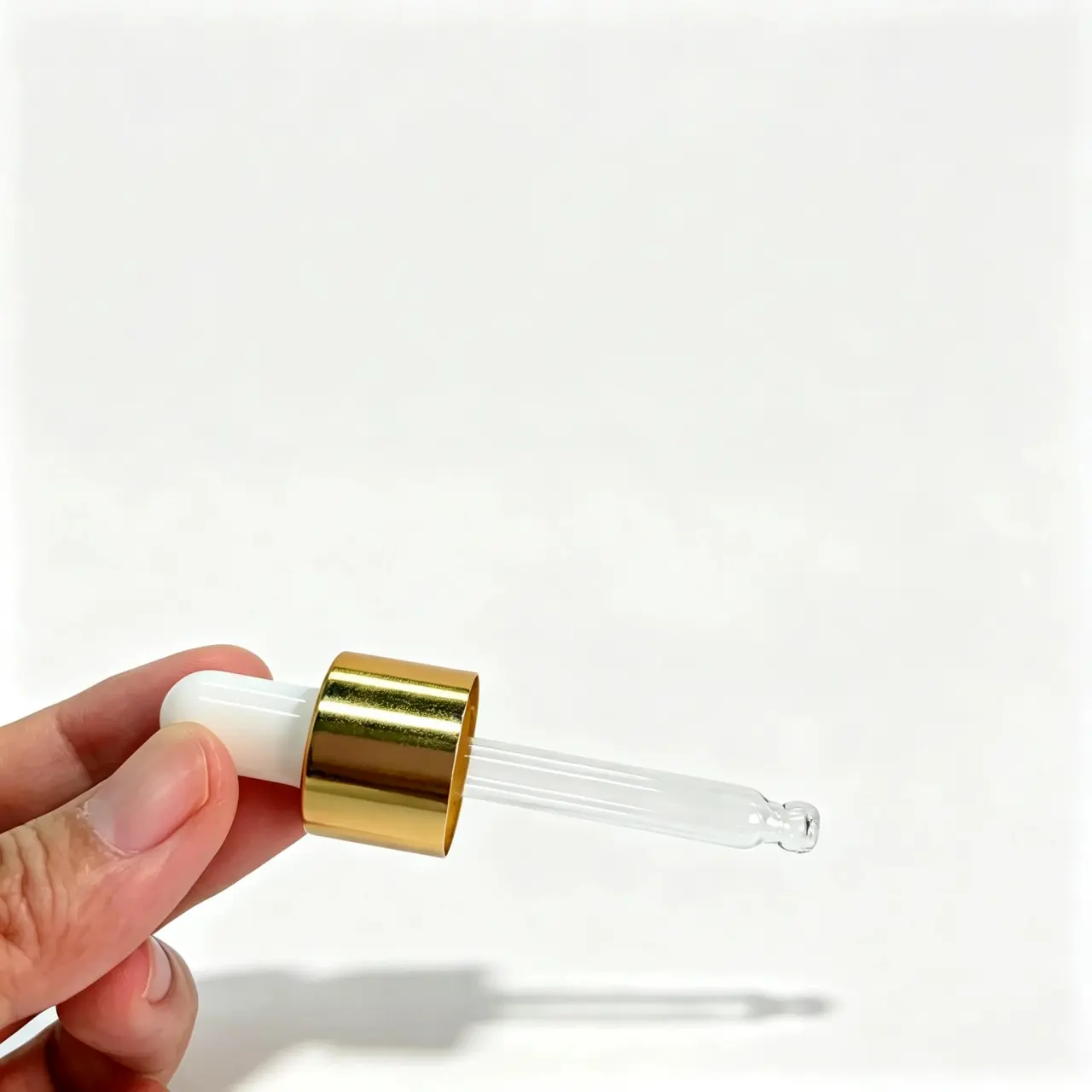 Vue de côté de la pipette compte-gouttes à collerette en aluminium doré Profil latéral de la pipette compte-gouttes à collerette en aluminium doré montrant la poire en caoutchouc blanc, la collerette métallique et le tube en verre